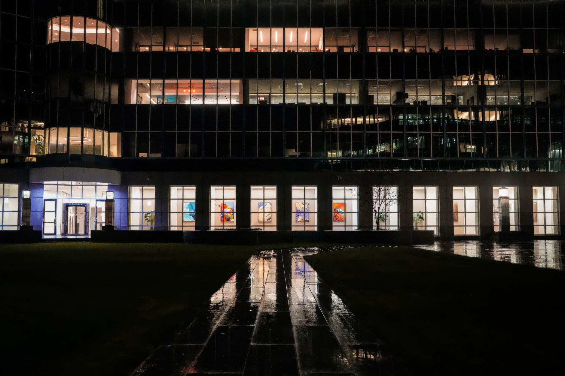 Office building at night with lit windows and a wet path